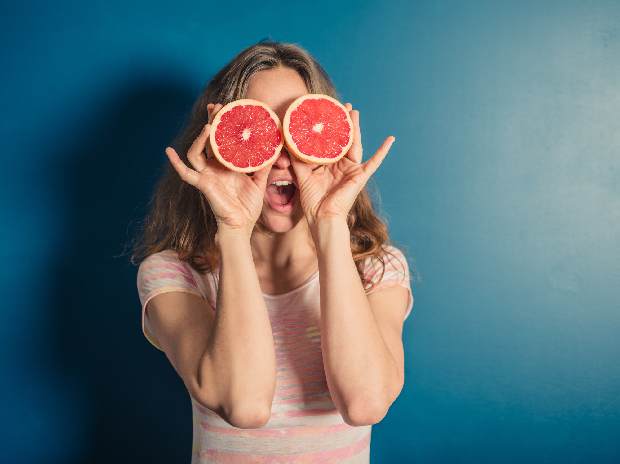 A young woman is using two halves of a grapefruit as binoculars